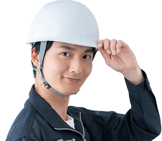 白いヘルメットを手で押さえ、微笑む若手作業員