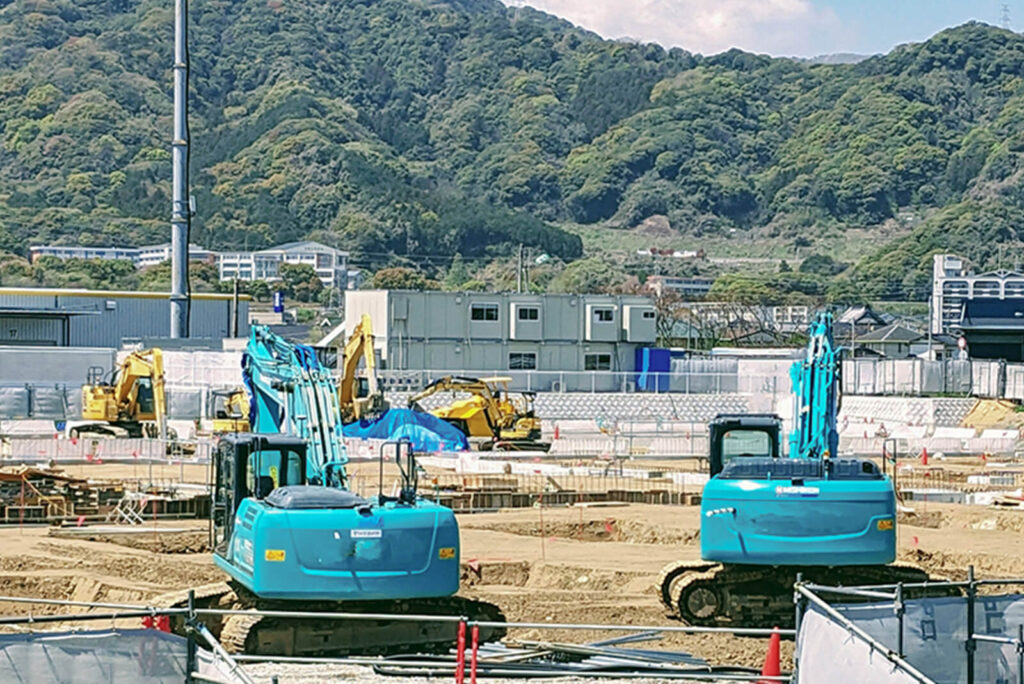 山を背景に複数の重機が稼働する大型建設現場