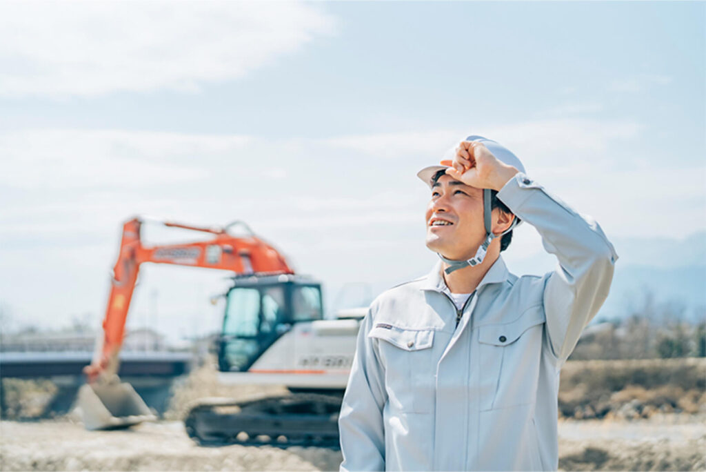 建設現場でヘルメットをかぶり、笑顔で空を見上げる作業員